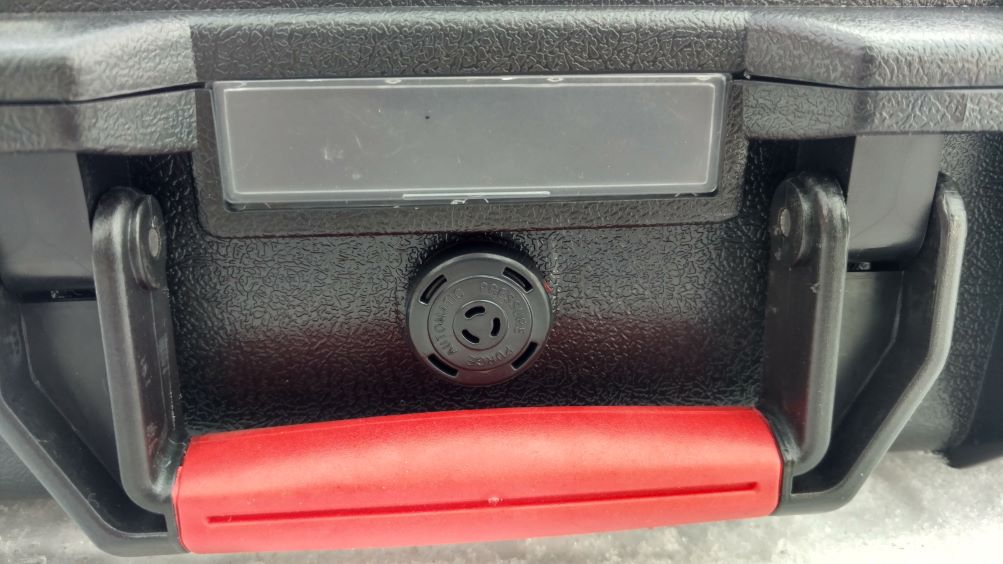  Close-up of a black and red suitcase handle, featuring a pressure valve for secure storage.