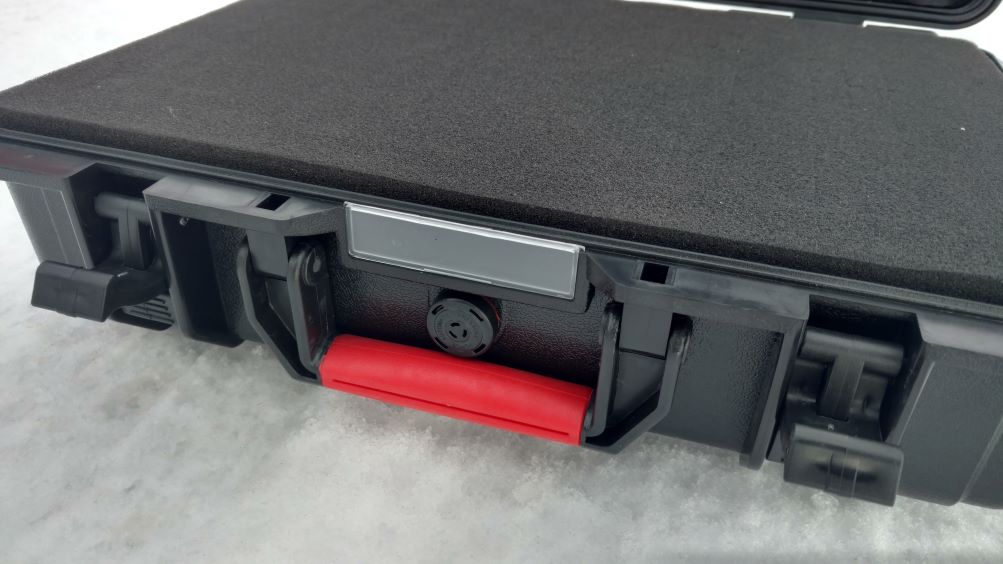 A sturdy black gun case with prominent red handles and a pressure valve.