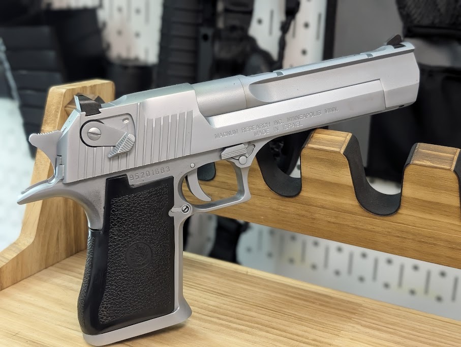 A silver pistol displayed on a polished wooden stand, showcasing its sleek design and craftsmanship.